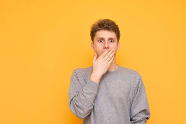 Genç adam kameraya sarı bir arka plan üzerinde seyir sürpriz, eliyle kaplı. Duygusal adam hayretle kameraya bakıyor. Boşaltmak