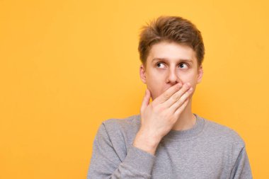 Yakın çekim portre, eliyle ağzını kapsayan bir sürpriz çocuğun duygusal boşaltmak, izole sarı arka plana benziyor. Sürpriz sarı bir arka plan üzerinde duran, uzakta arayan genç bir adam
