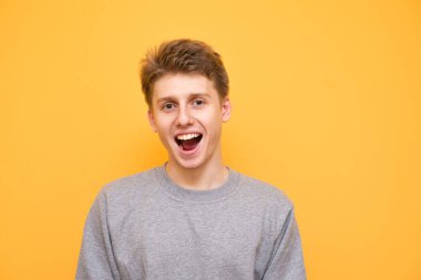 Yakın çekim portre sarı bir arka plan üzerinde duran ve kameraya bakarak bir gri sweatshirt gülümseyen bir çocuk. Sarı bir arka plan üzerinde olumlu genç Genç pozlar.