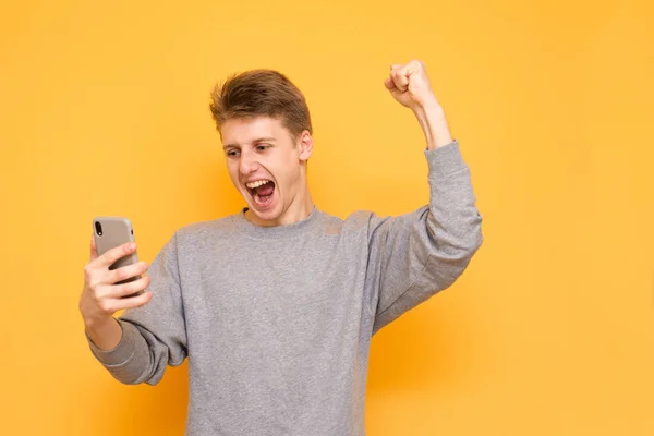 Positive Young Man Holds Smartphone His Hands Looks Screen Rejoices — Stock Photo, Image
