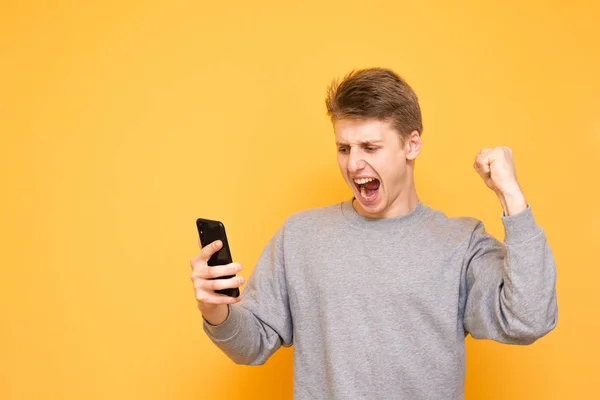 Expressive Guy Casual Clothing Looks Smartphone Screen Rejoices Hands Yellow — Stock Photo, Image
