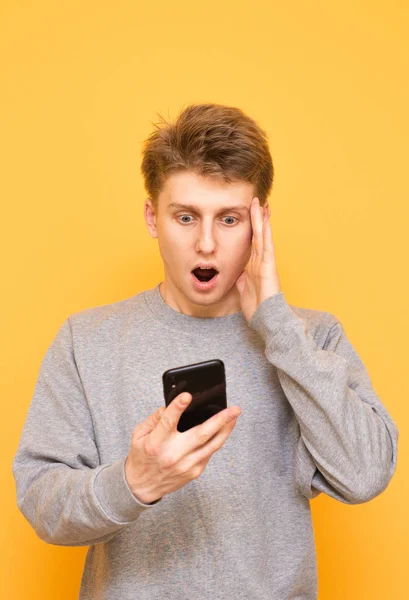 Shocked Guy Uses Smartphone Yellow Background Looks Screen Astonished Look — Stock Photo, Image