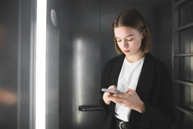 Siyah takım elbiseli ciddi çalışan mesajlar onun akıllı Asansör kontrol ediyor. Akıllı kadın memur patronu asansörde mesaj atıyor.