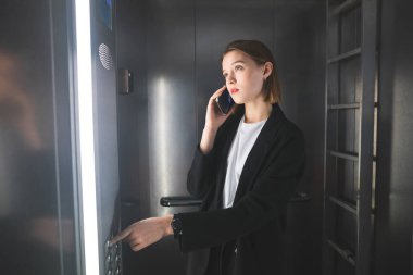 Genç Avrupa ofis çalışanı kat Asansör sayısı bakarak ve Evet. Asansör düğmesine basarak telefon işkadını bitti.