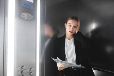 Kesinlikle işkadını asansörde belgeleri holding kameraya bakarak bıkmış. Kağıtları asansörde holding ve iş yerinde problemleri sinirli kadın ofis çalışanı. Kadın kafasını dokunmadan.