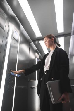 Bir elinde smartphone ve laptop başka bir holding Asansör düğmesine basarak ciddi iş kadını. İşçisi kadın ofis Asansör düğmesine basıyorum ve becerikli alet onun elinde tutan.