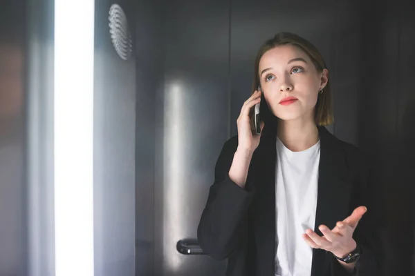 Fröhliche Geschäftsfrau Die Fahrstuhl Schicken Schwarzen Anzug Telefon Etwas Erklärt — Stockfoto