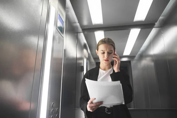 Serious Businesswoman Talking Phone Looking Papers Elevator Young Female Employee — Stock Photo, Image