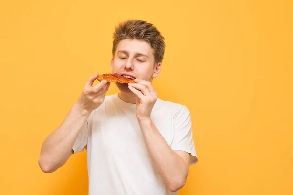 Tânărul Mănâncă Bucată Pizza Apetisantă Fundal Galben Tipul Flămând Ține — Fotografie, imagine de stoc