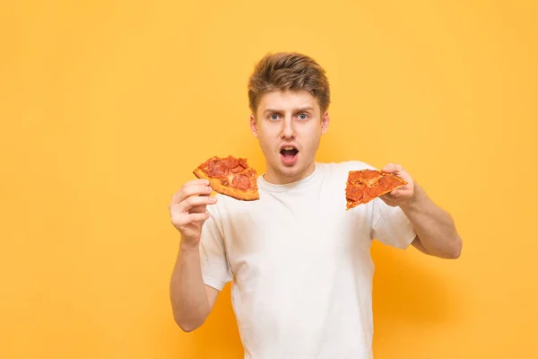 Tânăr Uimit Fundal Galben Ținând Două Bucăți Pizza Mâini Uitându — Fotografie, imagine de stoc