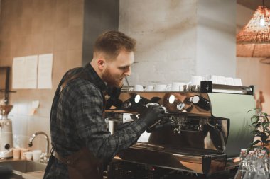 Sakallı genç barista kahve makinesi kahve dükkanında temizliyor. Barmen kafede kahve makinesi hazırlama.