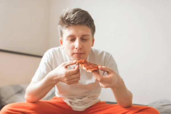 彼の手でピザの部分でベッドに座っている男の近くに縦目を食べて終了 ファーストフード ピザのコンセプト 若い男は 朝食にピザを食べる — ストック写真