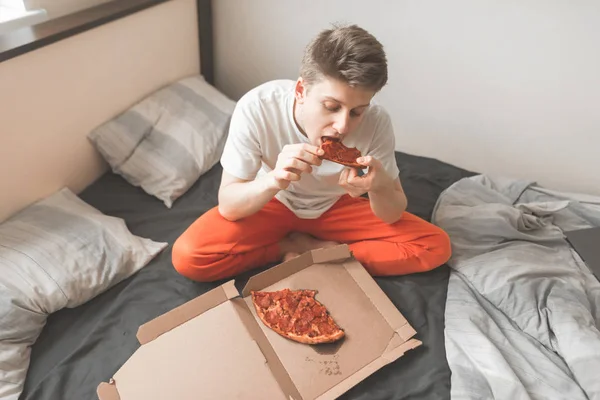 Jovem Feliz Sentado Casa Uma Cama Com Uma Caixa Pizza — Fotografia de Stock