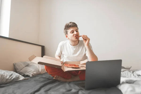 Der Junge Mann Sitzt Auf Einem Bett Mit Pizzaschachtel Und — Stockfoto