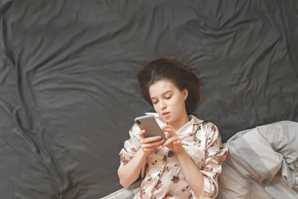 Дівчина Легкій Піжамі Відпочиває Ліжку Спальні Використовуючи Смартфон Орієнтований Екран — стокове фото