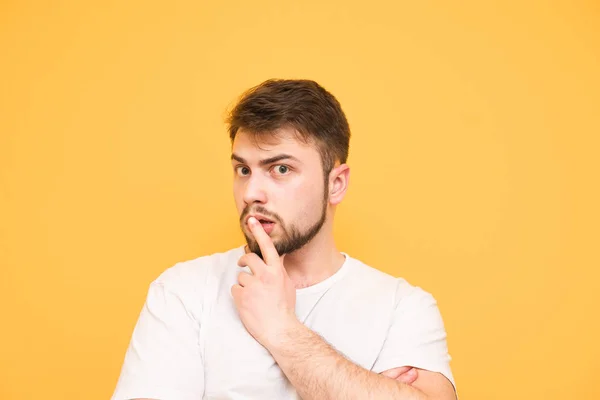 Hombre sorprendido en una camiseta blanca sobre un fondo amarillo sostiene hi — Foto de Stock