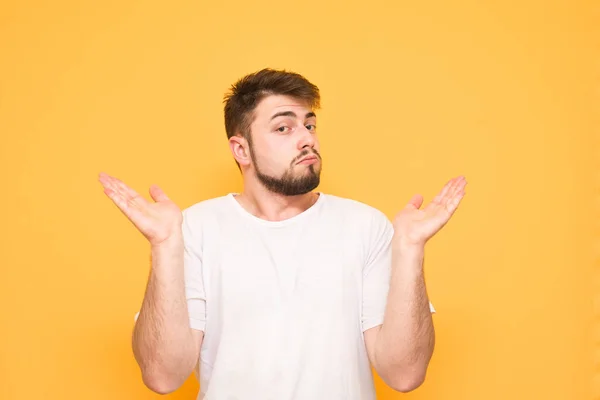 Homem confuso com uma barba em um fundo amarelo, tendo levantado — Fotografia de Stock