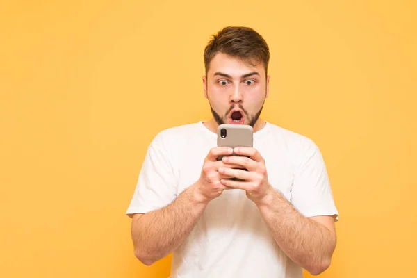Shock man con una barba, mirando en la pantalla del teléfono inteligente y wond — Foto de Stock