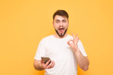 Şaşırmış adam beyaz bir T-shirt bir akıllı telefon elinde tutar.