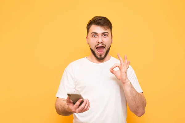 Surprised man in a white T-shirt holds a smartphone in his hands — Stock Photo, Image