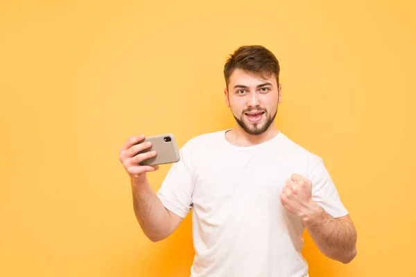 Ευτυχισμένος άνθρωπος με ένα smartphone στο χέρι του, φορώντας ένα άσπρο T-shirt — Φωτογραφία Αρχείου