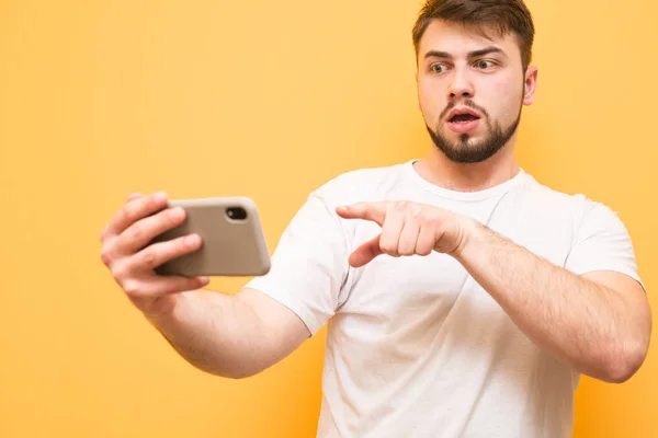 Surprised man uses a smartphone on a yellow background, looking — Stock Photo, Image