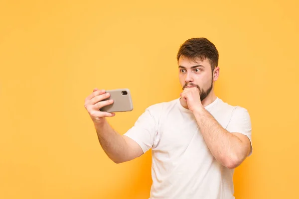 Shocked man dressed in a white T-shirt stands on a yellow backgr