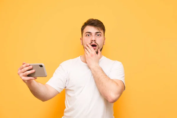 Shocked man with a beard standing on a yellow background with a — Stock Photo, Image
