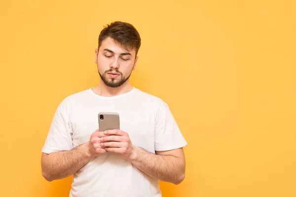 Hombre tranquilo con barba sobre fondo amarillo, utiliza un smartphone , — Foto de Stock