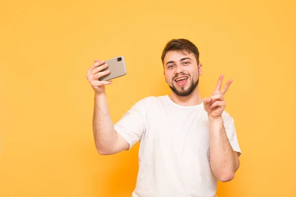 Adult male in a white T-shirt takes selfie on a yellow backgroun — Stock Photo, Image