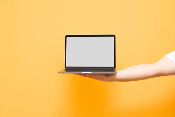 Mano maschile tiene un computer portatile con uno schermo bianco su un backgro giallo — Foto Stock