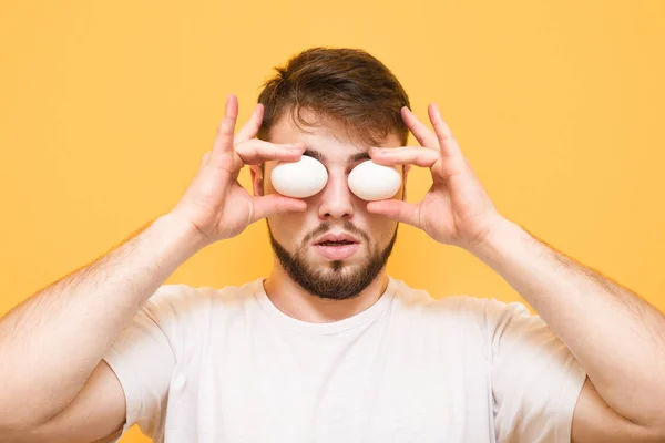 Man stands on a yellow background and holds eggs at the level of