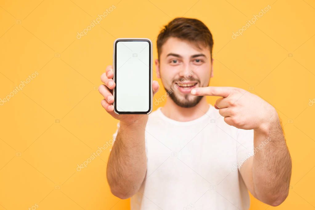 Smiling man holds a smartphone in his hands, and shows his finge