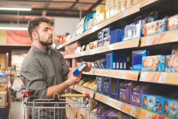 El hombre está en un supermercado con un paquete de galletas en su han — Foto de Stock