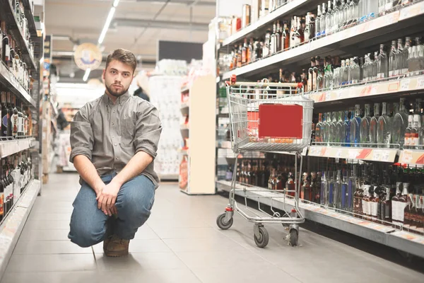 Jonge man kijkend naar fles wijn in supermarkt — Stockfoto