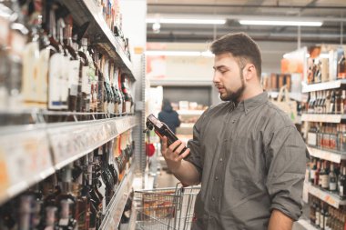 Sakallı adam elinde bir şişe konyak ile bir süpermarket duruyor, etiket bakıyor ve okur. Yetişkin süpermarkette güçlü alkol departmanı seçer. Mağazada alkol