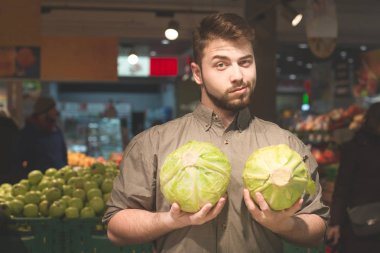 Elinde iki lahana ile bir süpermarket sebze bölümünde duran bir adamın portresi, kameraya bakıyor. bir süpermarkette abbage alıcı.