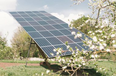 Bahar konsepti. Bahçede ev güneş panelleri arka planda çiçek açan ağaçlar. Yeşil güneş enerjisi. Fotovoltaik, alternatif elektrik kaynağı