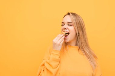 Aç çekici kız, bir sürü patates kızartması yiyor, aperatifler bir avuç tutar ve ağzına koyar. Bir kızın yakın çekim portresi, sarı bir arka planda kızarmış patates yiyor
