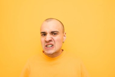 Parlak kıyafetlerle karizmatik bir adamın portresi, sarı bir arka planda agresif bir yüz yapar ve kameraya bakar. Dişleri üzerinde Grillz ile Evil şık adam kameraya pozlar. Izole