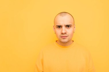 Kel bir kafa ve küpe ile şaşkın genç adam sarı bir arka plan üzerinde ve sarı rahat giyim giyen, kamera şaşırttı görünüyor. Boşaltmak