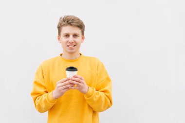 Hafif bir duvarın arka planına karşı elinde bir fincan kahve içeren mutlu adam. Parlak bir Casual giysi öğrenci beyaz bir arka planda elinde kahve ile pozlar, izole, sokak fotoğrafı