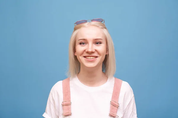 Κοντινό πορτρέτο μιας χαμογελαστή εφηβικής κοπέλας σε μπλε φόντο, φορώντας ένα μπλουζάκι, κοιτάζοντας μέσα στην κάμερα και πανηγυρίζοντας. Θετικό κορίτσι απομονώθηκε σε μπλε φόντο. — Φωτογραφία Αρχείου