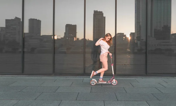 Menina loira elegante em uma camiseta branca com um pontapé rosa de scooter p — Fotografia de Stock