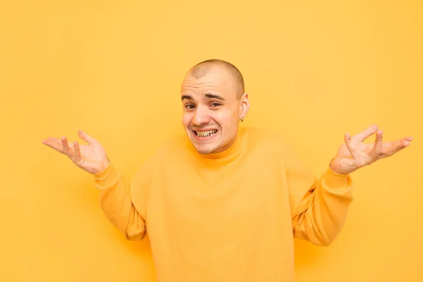 Portret van een grappige jonge man breekt zijn armen en kijkt in de camera, het dragen van een gele trui en Grillz op zijn tanden. Verwarde jongen op een gele achtergrond breekt zijn handen aan de zijkanten. — Stockfoto