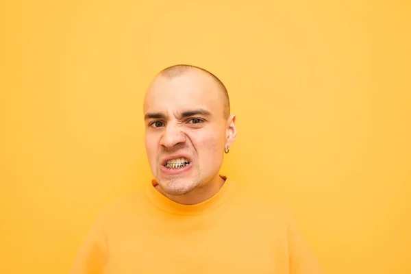 Portret van een charismatische man in heldere kleren maakt een agressief gezicht op een gele achtergrond en kijkt in de camera. Evil stijlvolle vent met Grillz op zijn tanden poseert voor de camera. Geïsoleerd — Stockfoto
