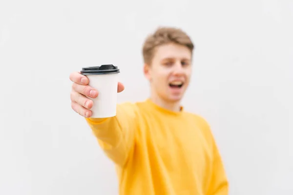 若い男の手にコーヒーと紙の白いカップ。明るいカジュアルな服を着た幸せな男は、彼の手にコーヒーのカップを保持し、笑顔。カップに集中しろコピースペース — ストック写真