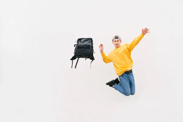 Elegante giovane uomo in un salto con uno zaino su uno sfondo bianco con indosso un abbigliamento casual luminoso. Studente con uno zaino in volo sullo sfondo di un muro bianco. Isolato. Copyspace . — Foto Stock