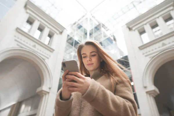 魅力的な女の子は、都市の近代的な建築の背景に手を保持し、スマートフォン上でインターネットを使用しています。スマートフォンを手に持った女性の都会的な肖像画。コピースペース — ストック写真