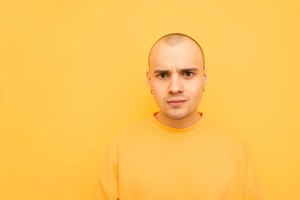 Baffled young man with a bald head and earrings is on a yellow background and looks surprised at the camera, wearing yellow casual clothing. Copyspace — Stock Photo, Image